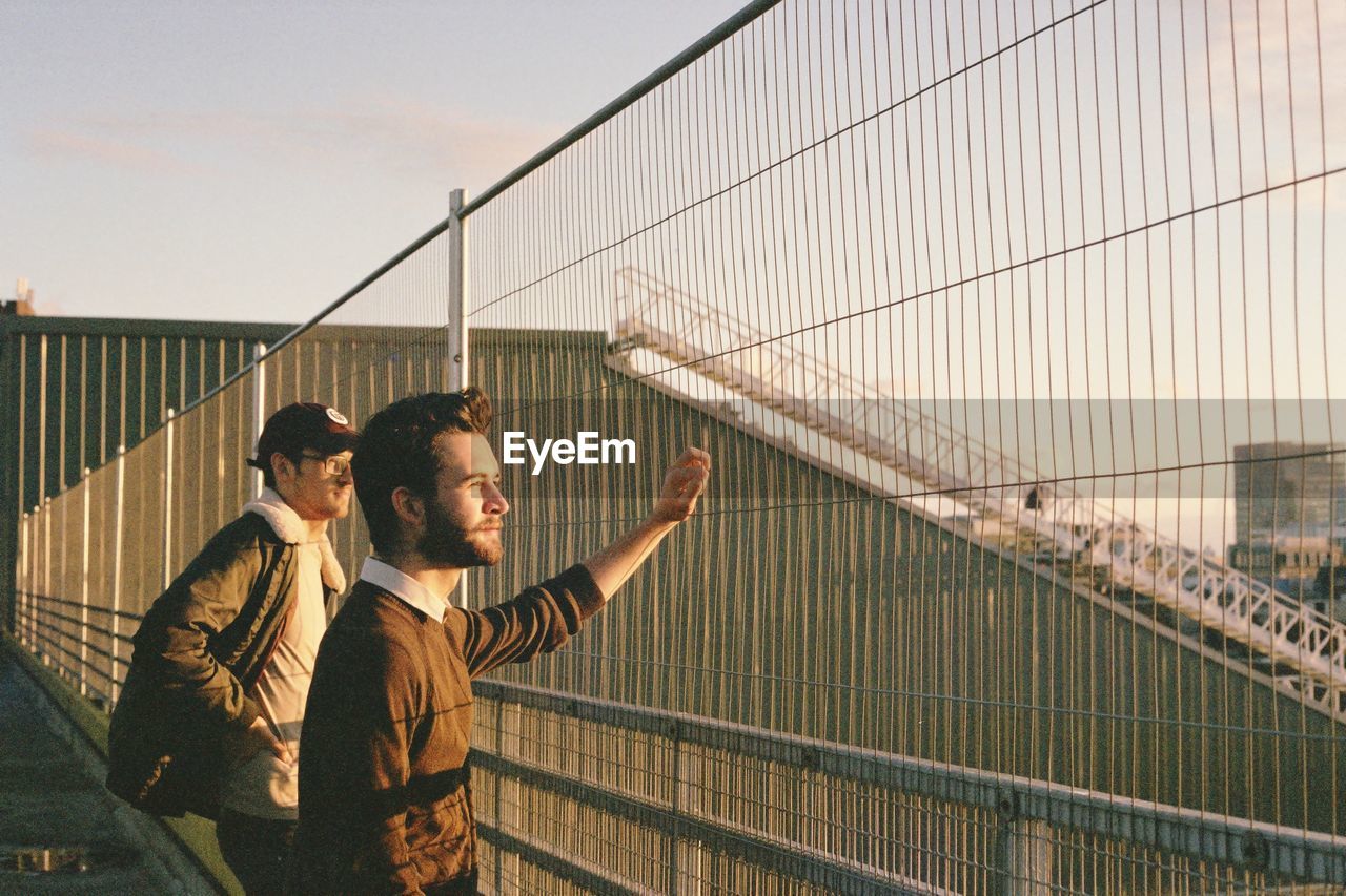 MEN STANDING BY RAILING AGAINST PEOPLE