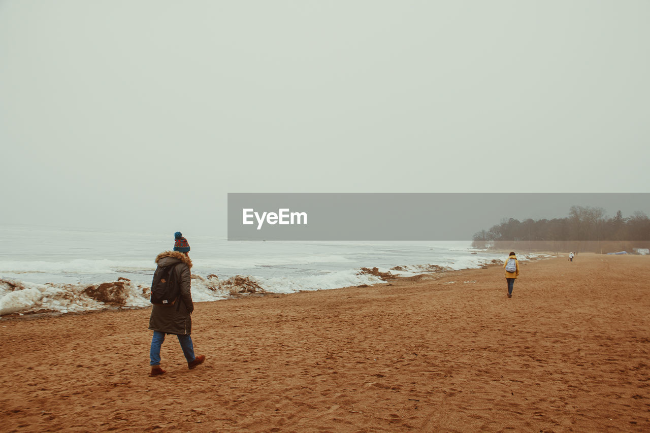 Rear view of woman walking on beach against clear sky