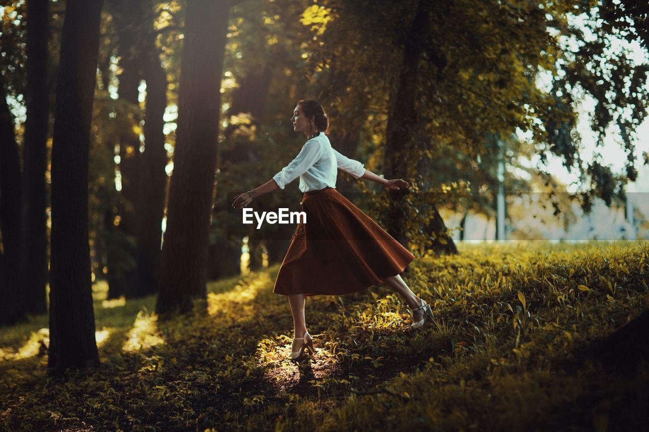 Side view of woman walking on field in forest