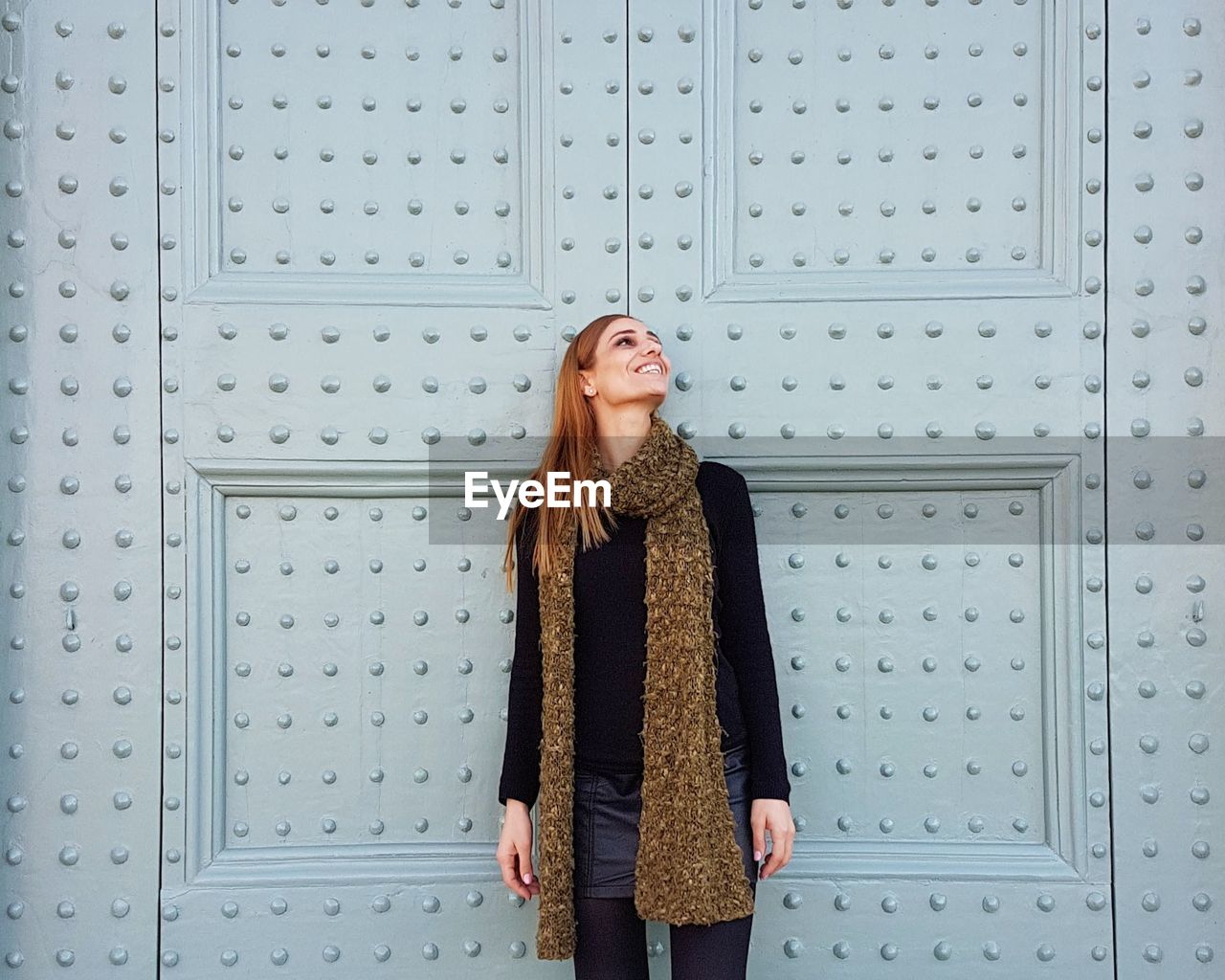 Young woman looking away while standing on wall / happy woman smiling