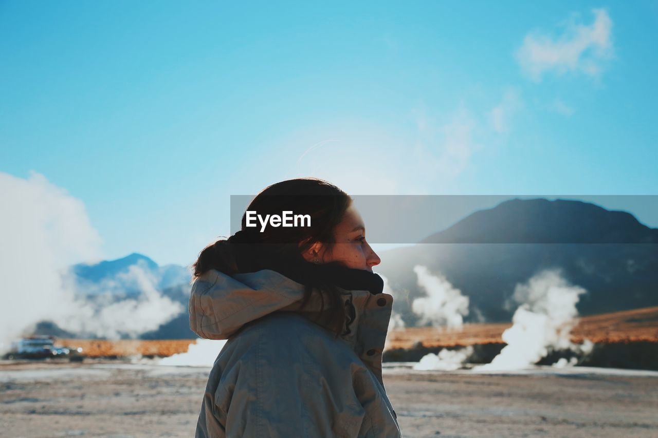 Profile view of woman wearing jacket while standing against blue sky