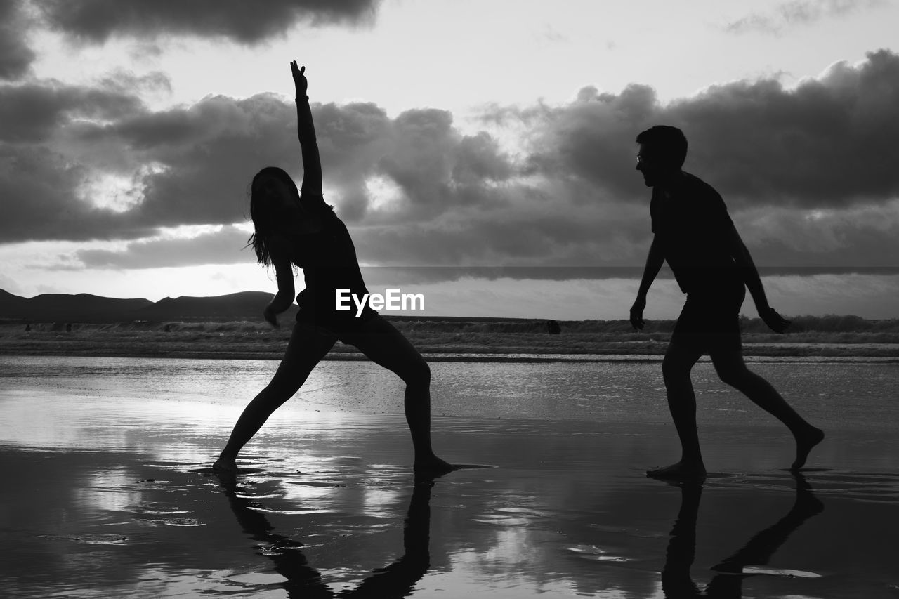 Silhouette couple standing on beach against sky