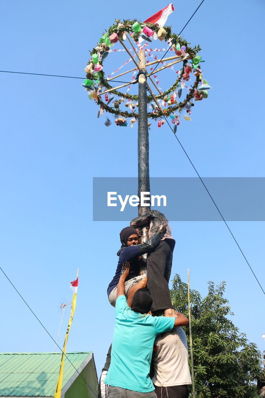 LOW ANGLE VIEW OF WOMAN HOLDING PLANT AGAINST BLUE SKY