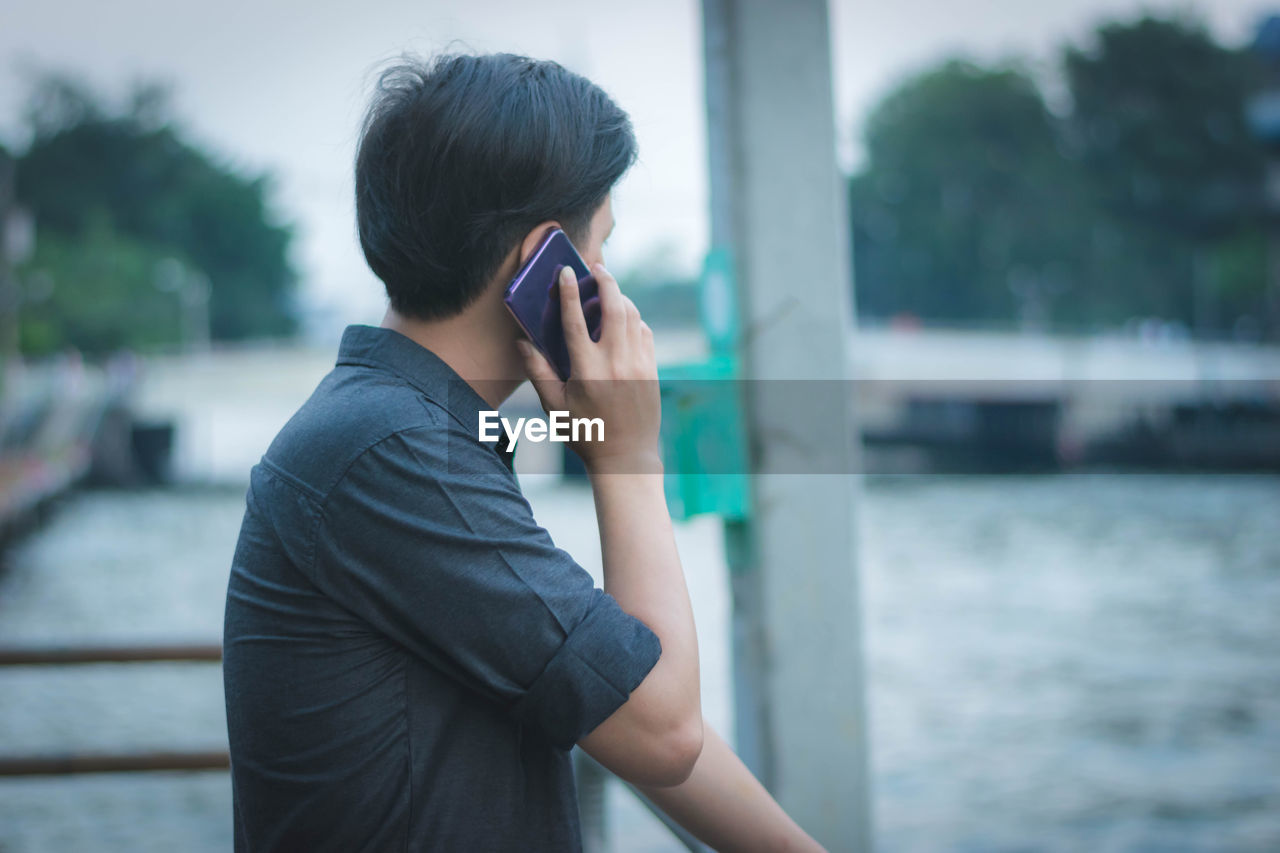 Man talking on mobile phone against pond