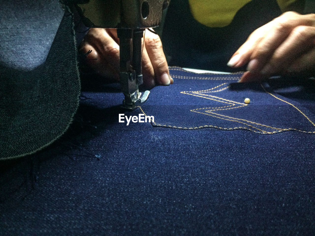 Cropped hands sewing jeans on machine
