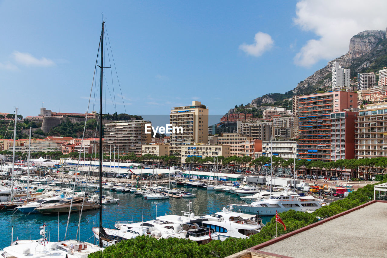 SAILBOATS MOORED AT HARBOR AGAINST BUILDINGS IN CITY