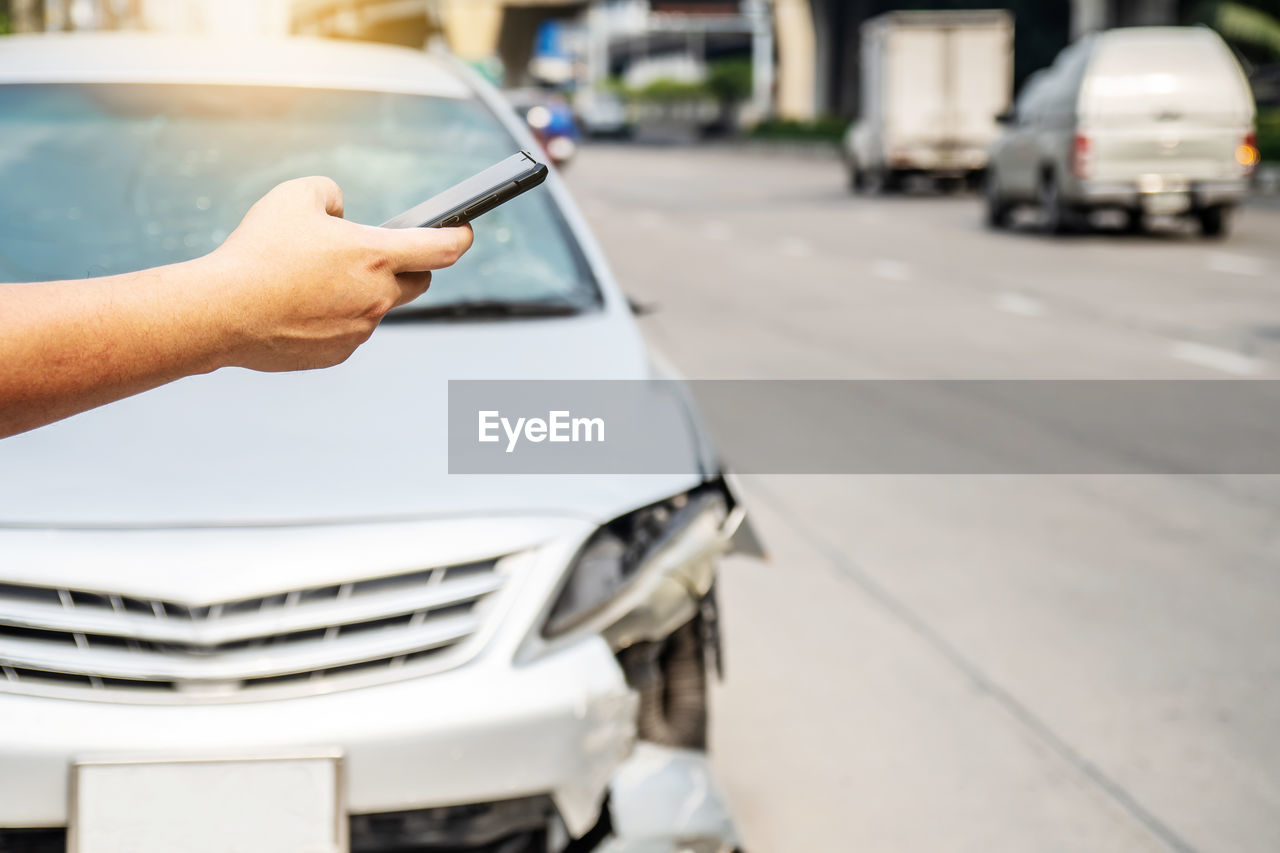 MIDSECTION OF MAN PHOTOGRAPHING CAR ON STREET