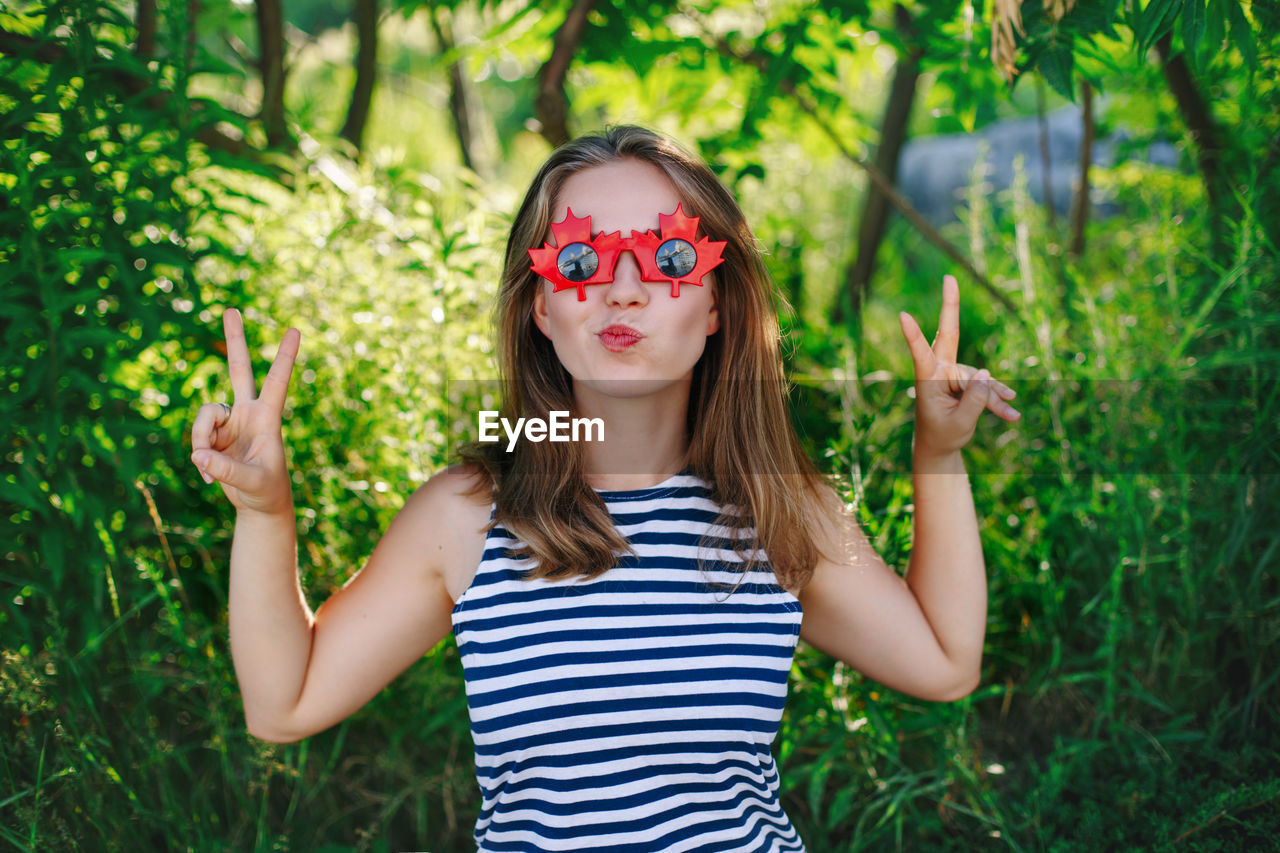 PORTRAIT OF WOMAN WEARING SUNGLASSES STANDING OUTDOORS