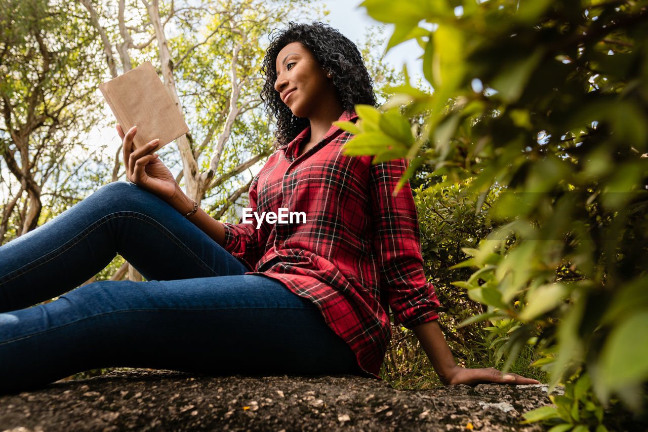 young woman using mobile phone while sitting against plants