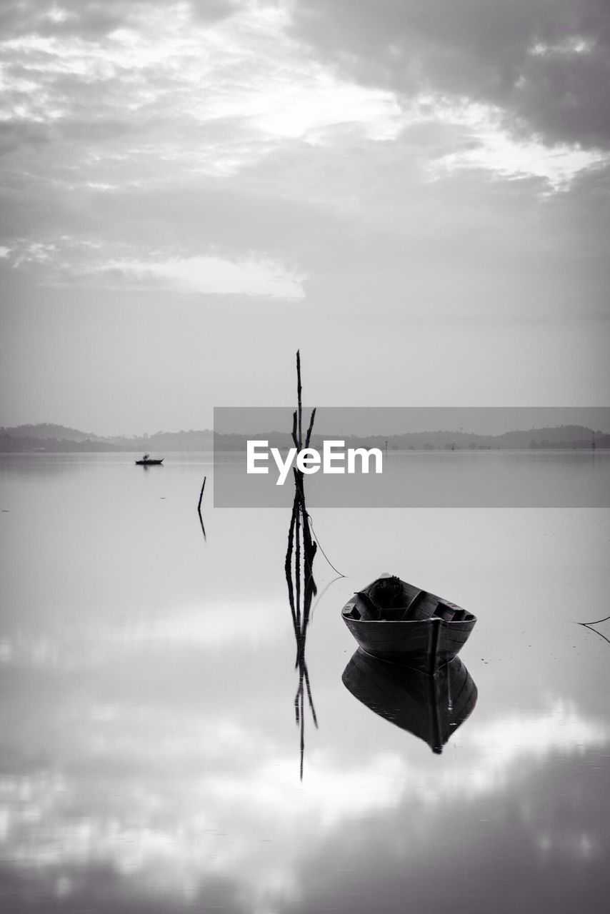 Reflection of boat moored in lake against cloudy sky