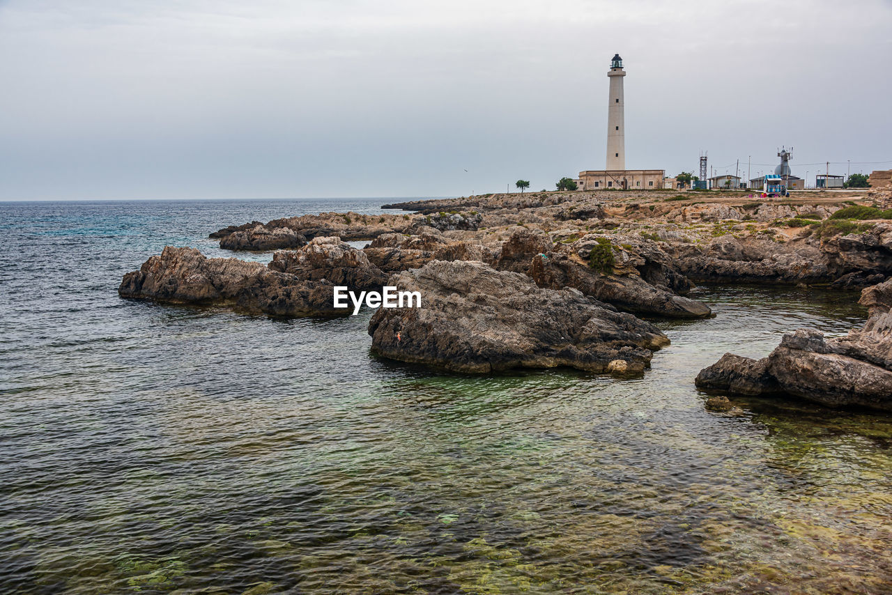 Lighthouse on rock by sea against sky