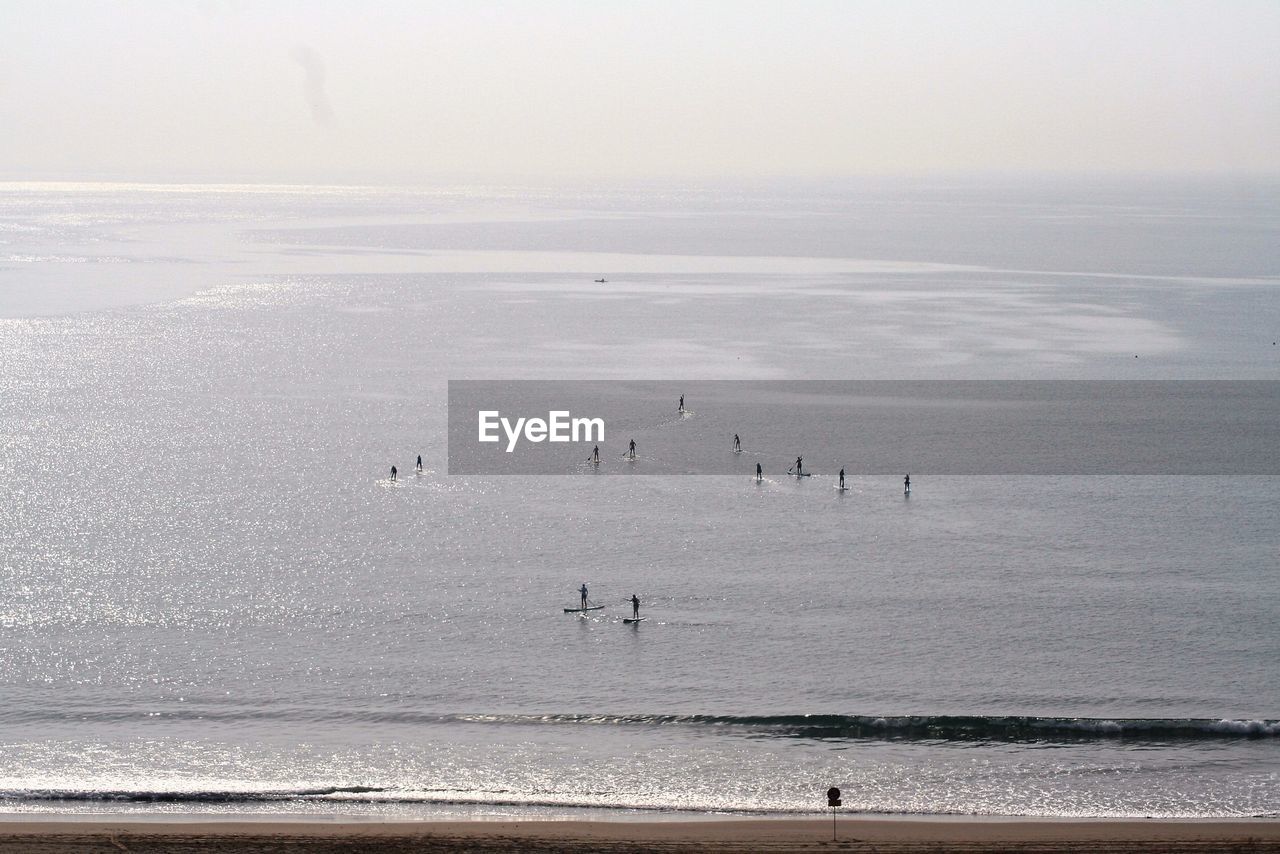 Distant view of people paddleboarding in sea against sky