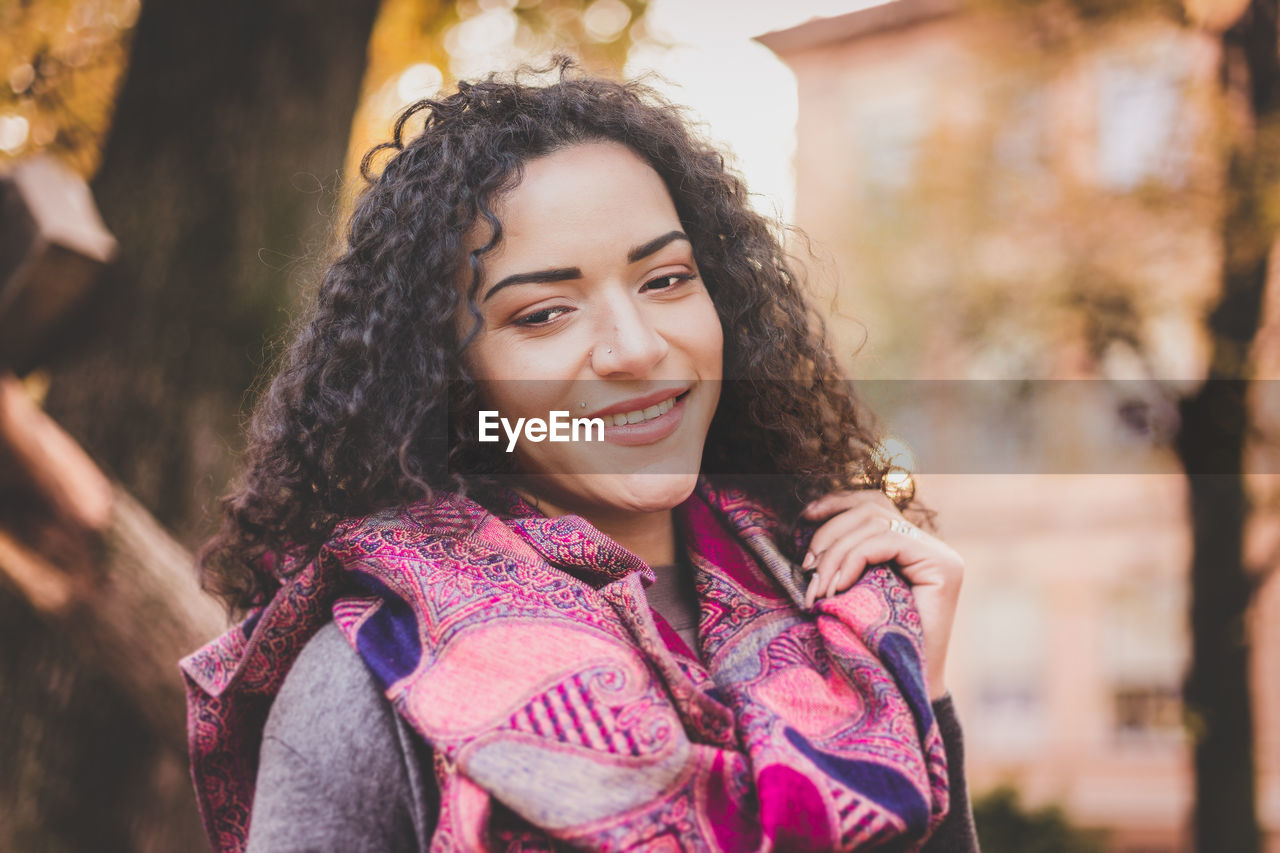 Close-up of smiling woman with curly hair standing outdoors