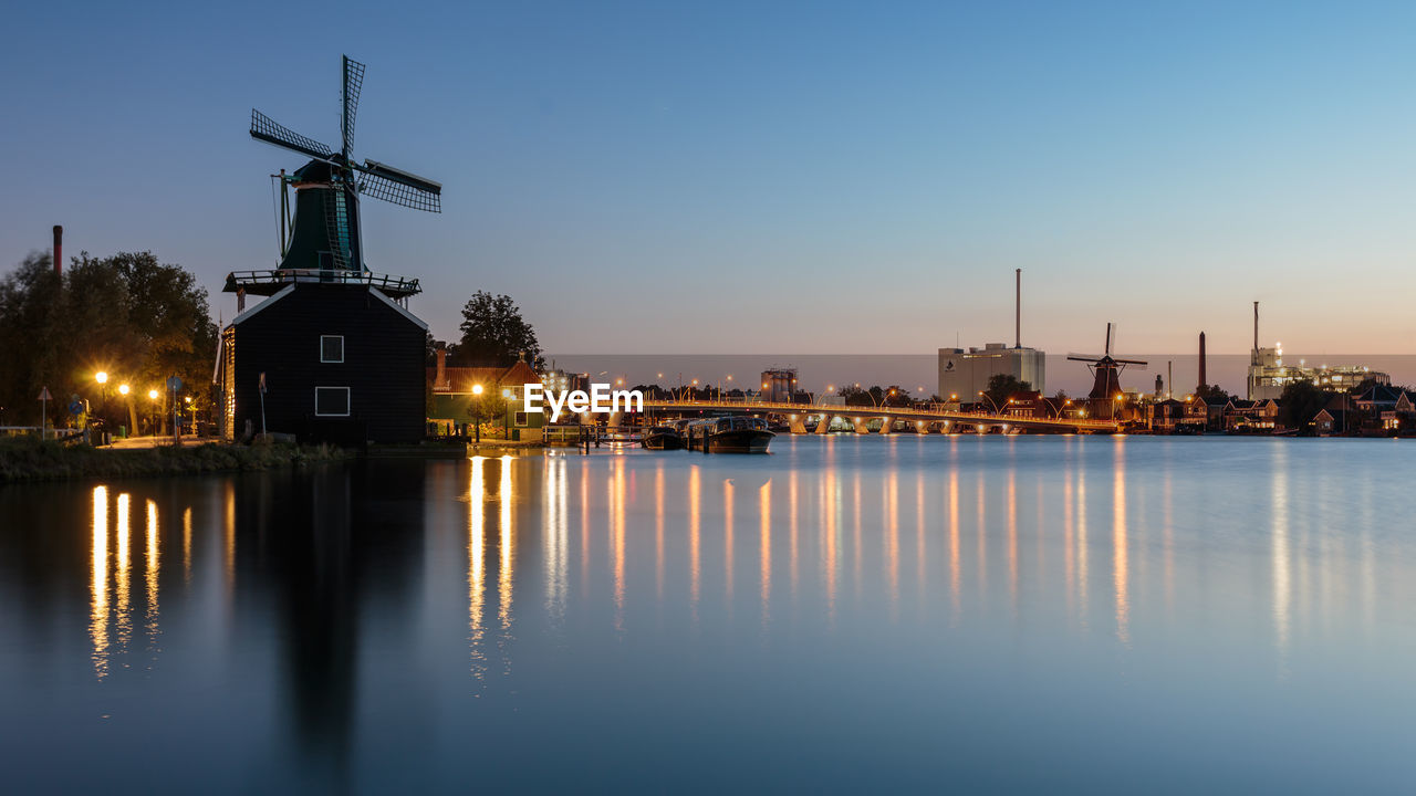 Traditional windmills by river against sunset sky