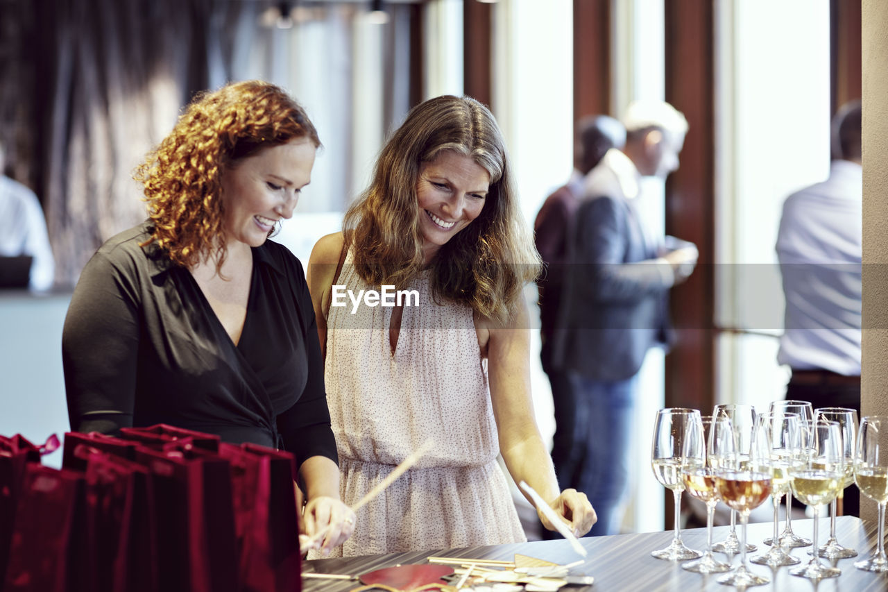 Smiling businesswomen looking at props by wineglasses on table in office party