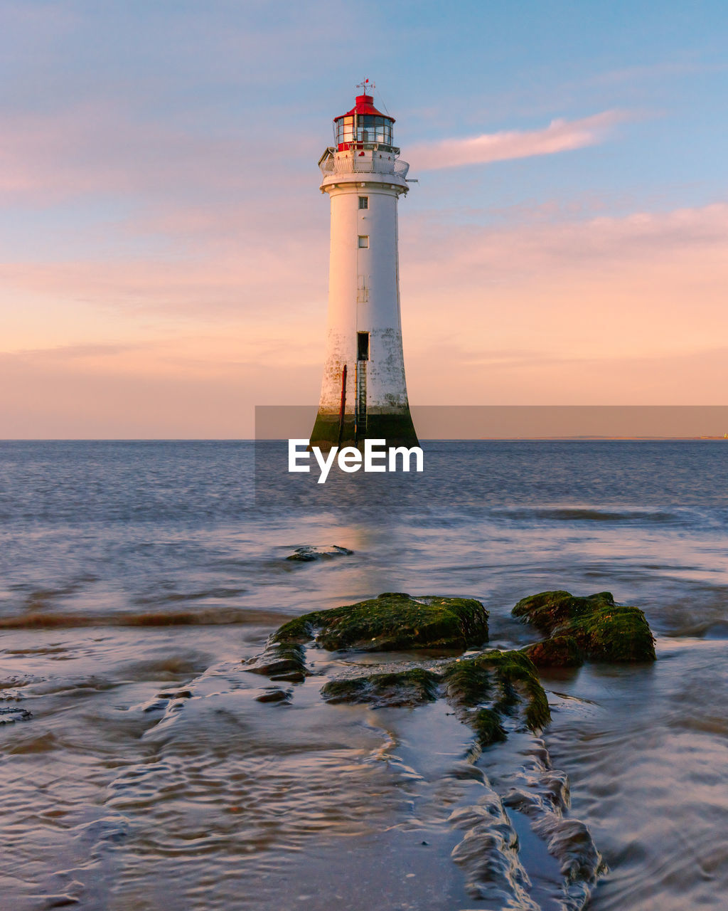 Lighthouse by sea against sky during sunset