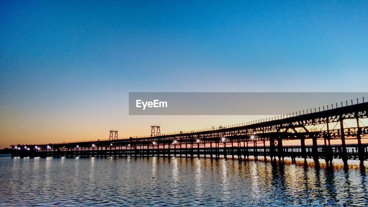 Bridge over calm river against clear sky at dusk