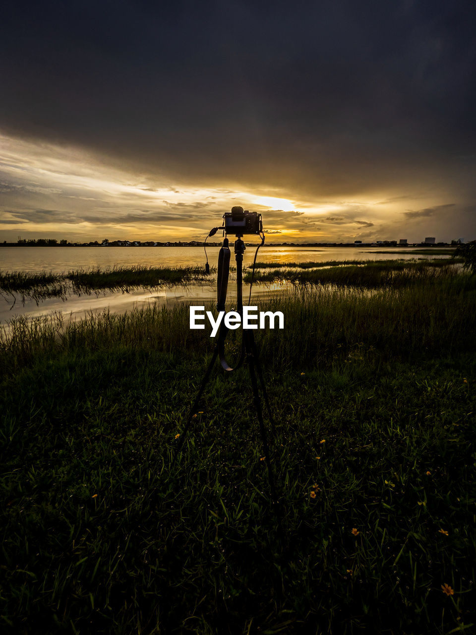 sky, sunset, nature, sunlight, evening, horizon, reflection, dawn, plant, land, grass, tripod, beauty in nature, field, cloud, landscape, environment, scenics - nature, water, light, camera, technology, darkness, rural scene, tranquility, occupation, outdoors, one person, sun, photographer, tranquil scene, agriculture, dramatic sky