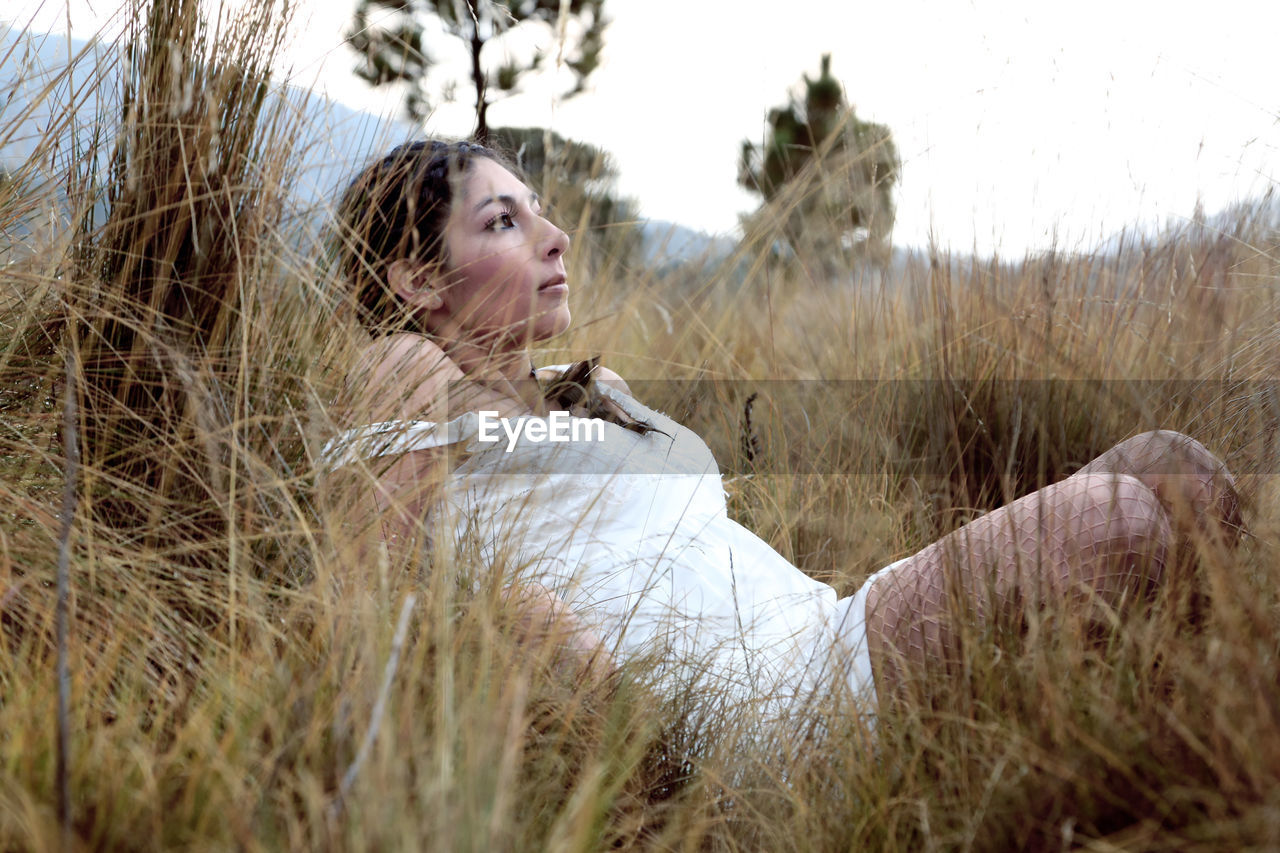 Beautiful woman looking away while lying on grassy field