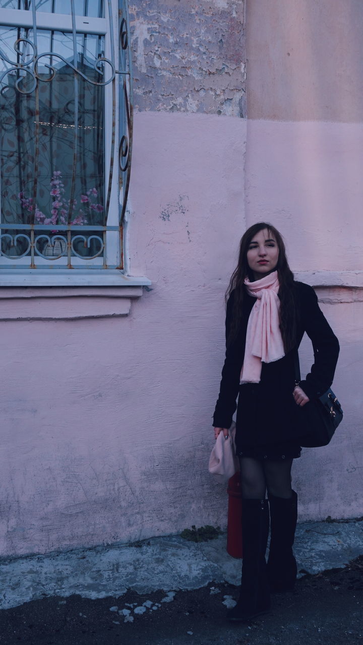 Young woman looking away while standing against building