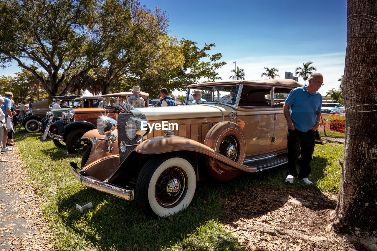 MAN STANDING BY CAR AGAINST TREE