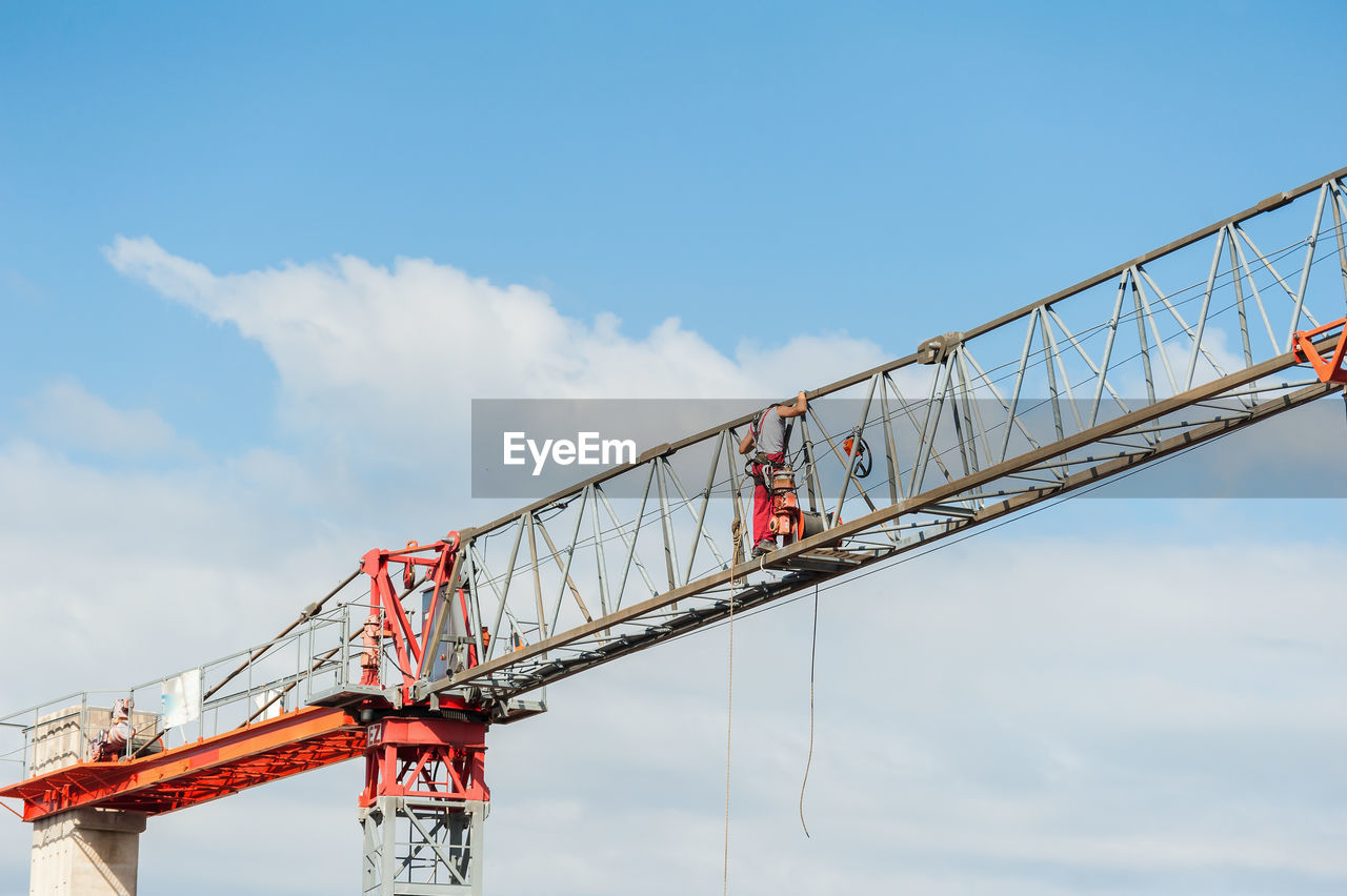 Low angle view of man standing crane against cloudy sky