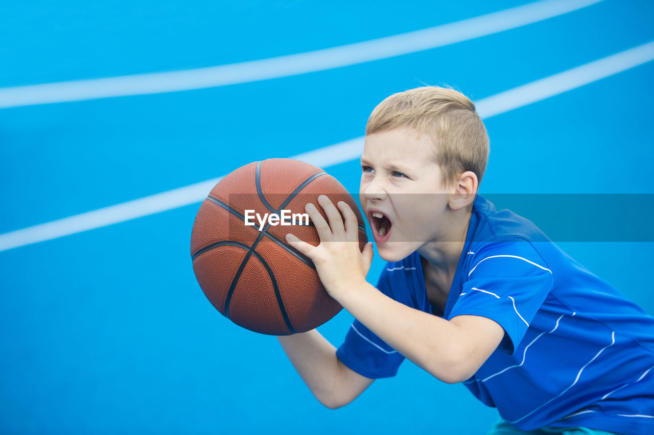 Boy with mouth open playing basketball on court