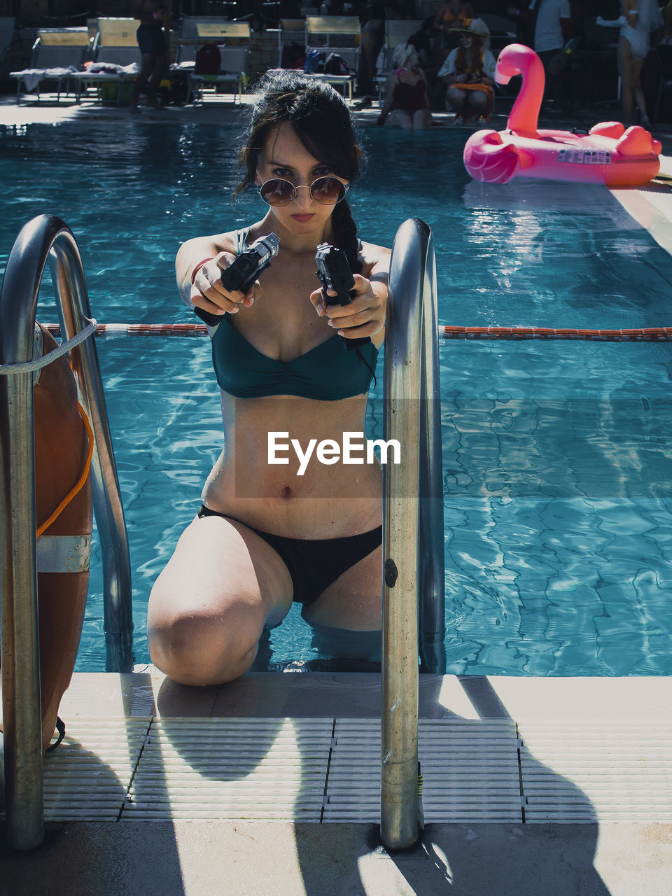 Portrait of woman aiming guns while standing in swimming pool