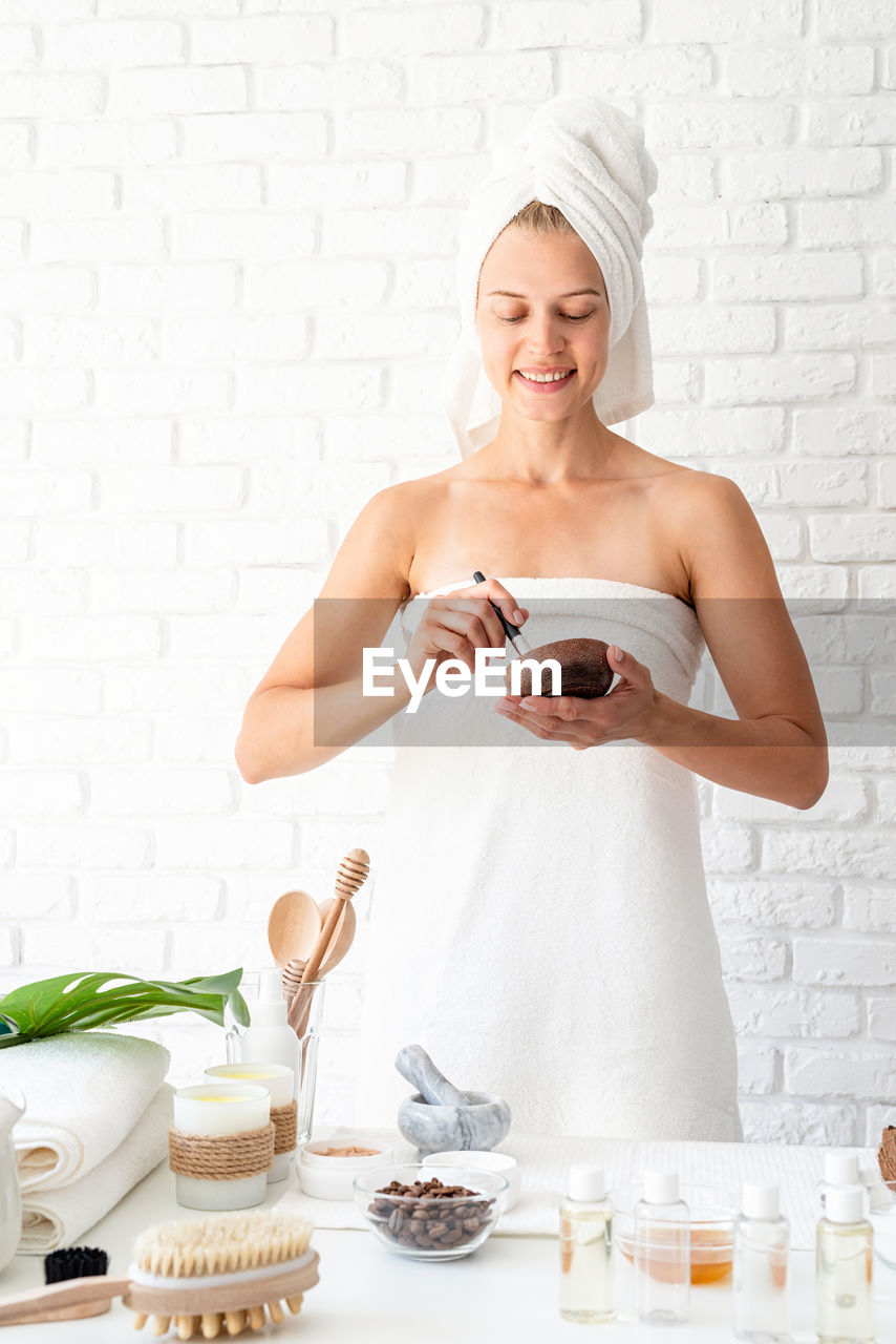 Young woman wearing white bathrobes towels on head doing spa procedures mixing natural ingredients