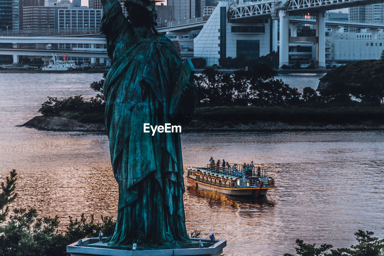 Statue in river with city in background