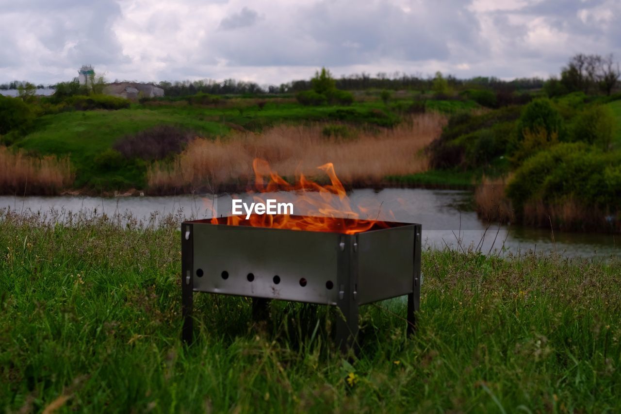 Fire burning in pit on grass against sky