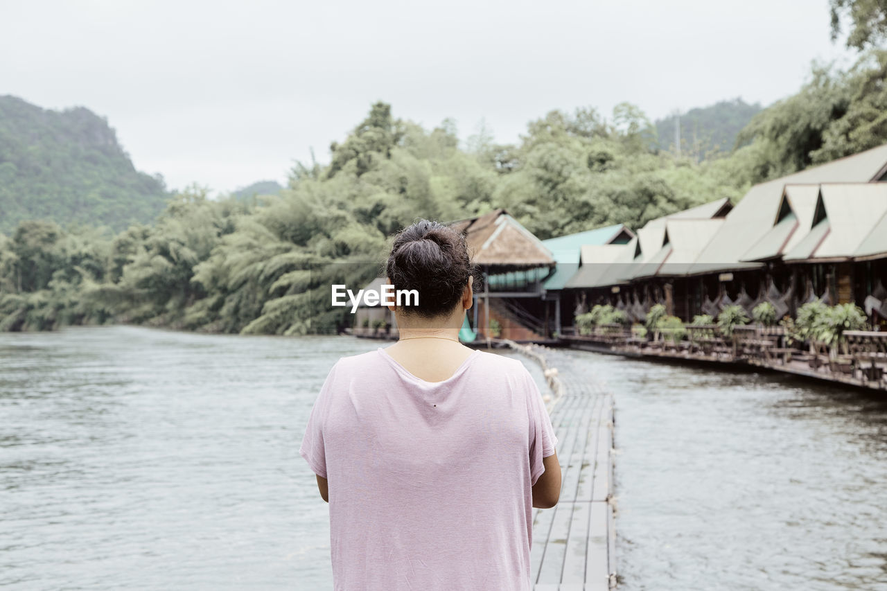 REAR VIEW OF MAN STANDING BY RIVER