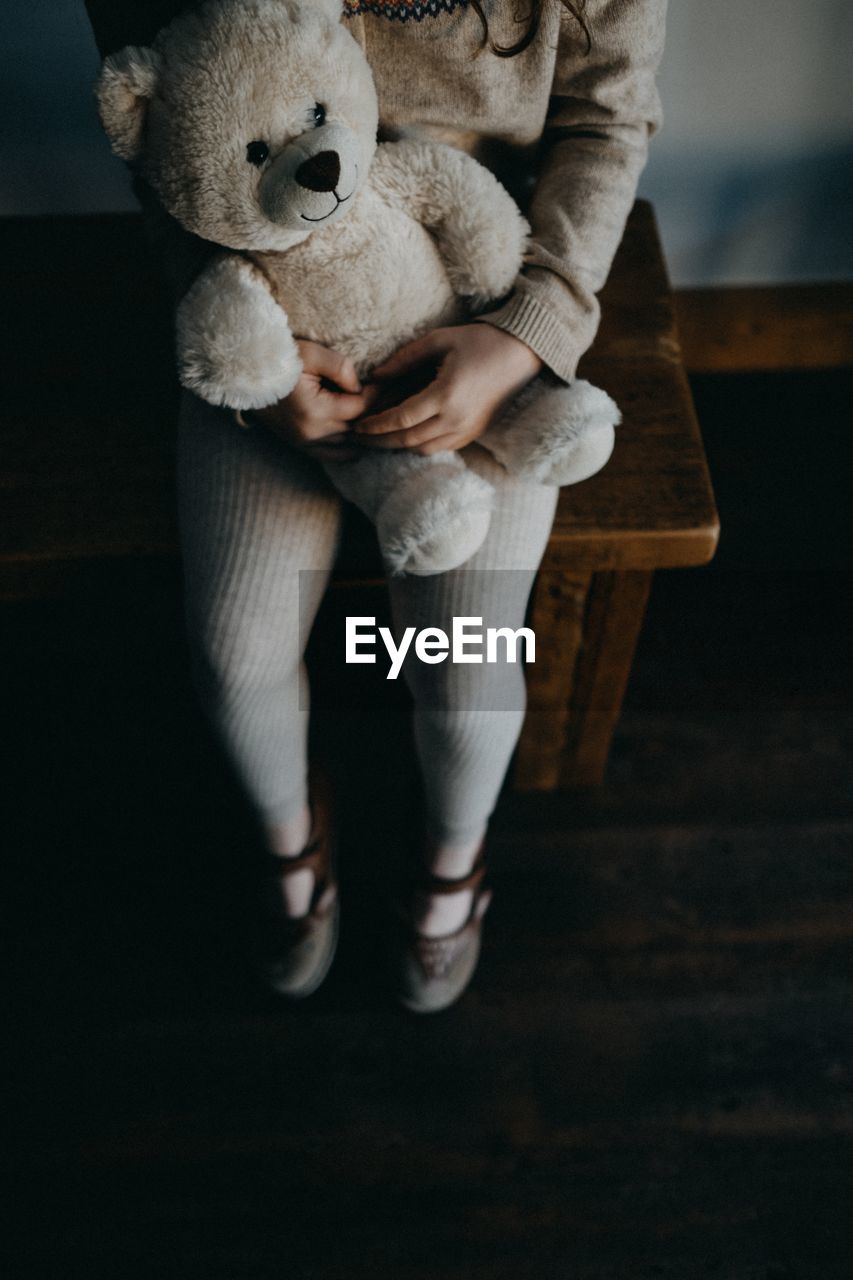 Low section of girl with stuffed toy sitting on table at home