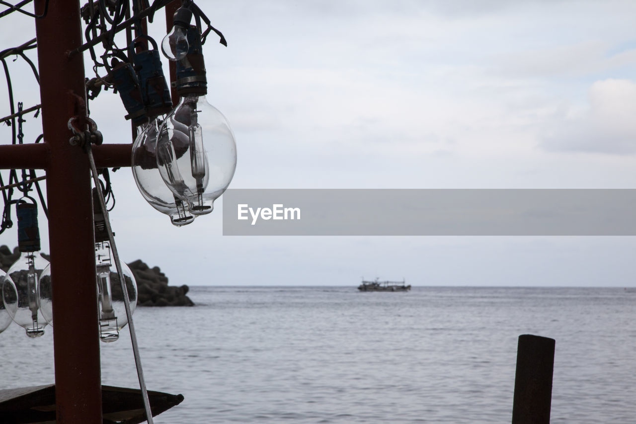 Light bulbs hanging on pole by sea against sky