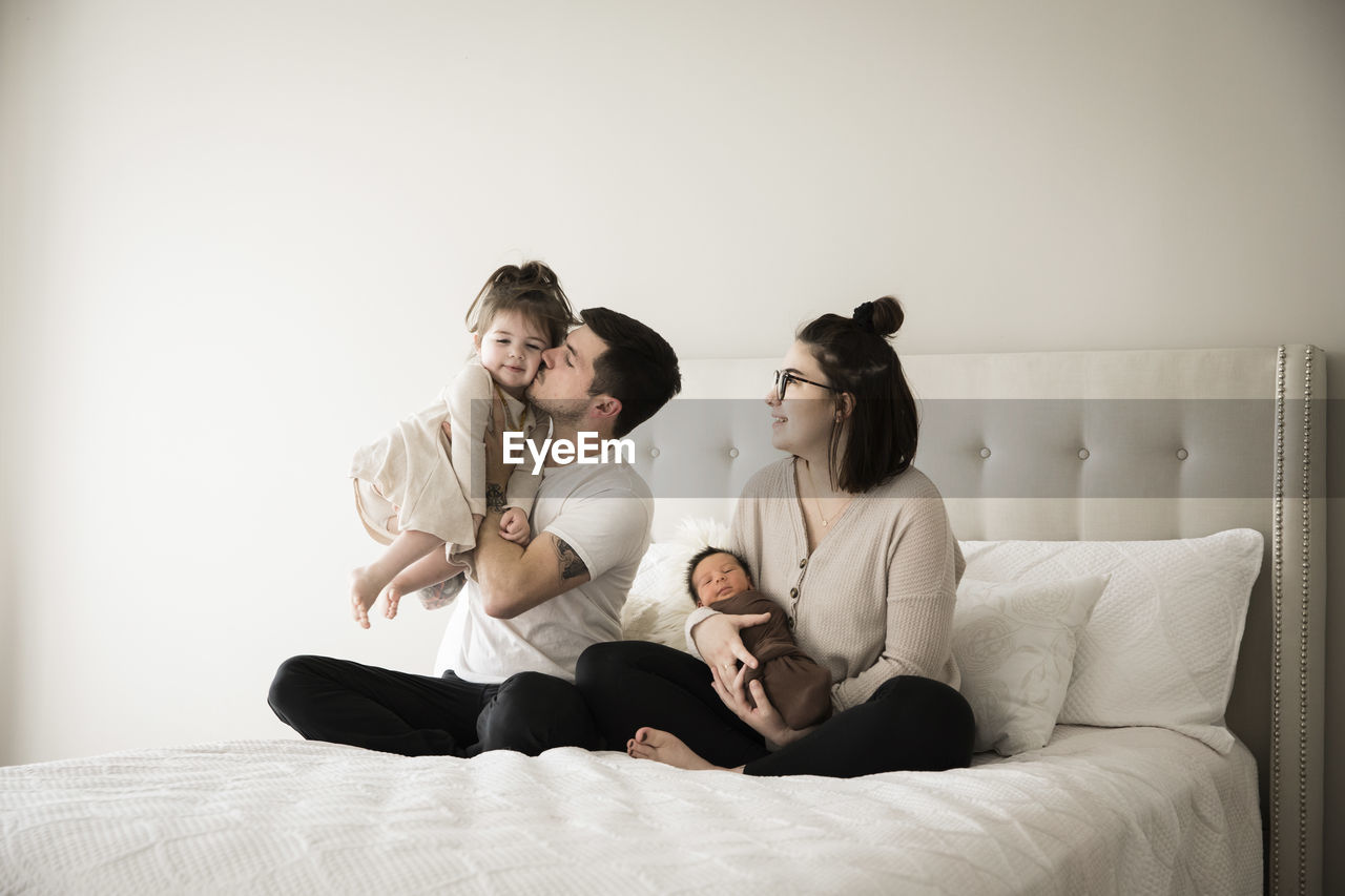 Millennial father kisses toddler daughter while sitting with family