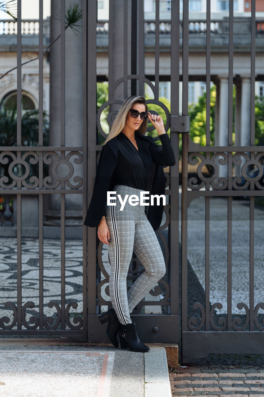 Portrait of woman wearing sunglasses standing against metal gate