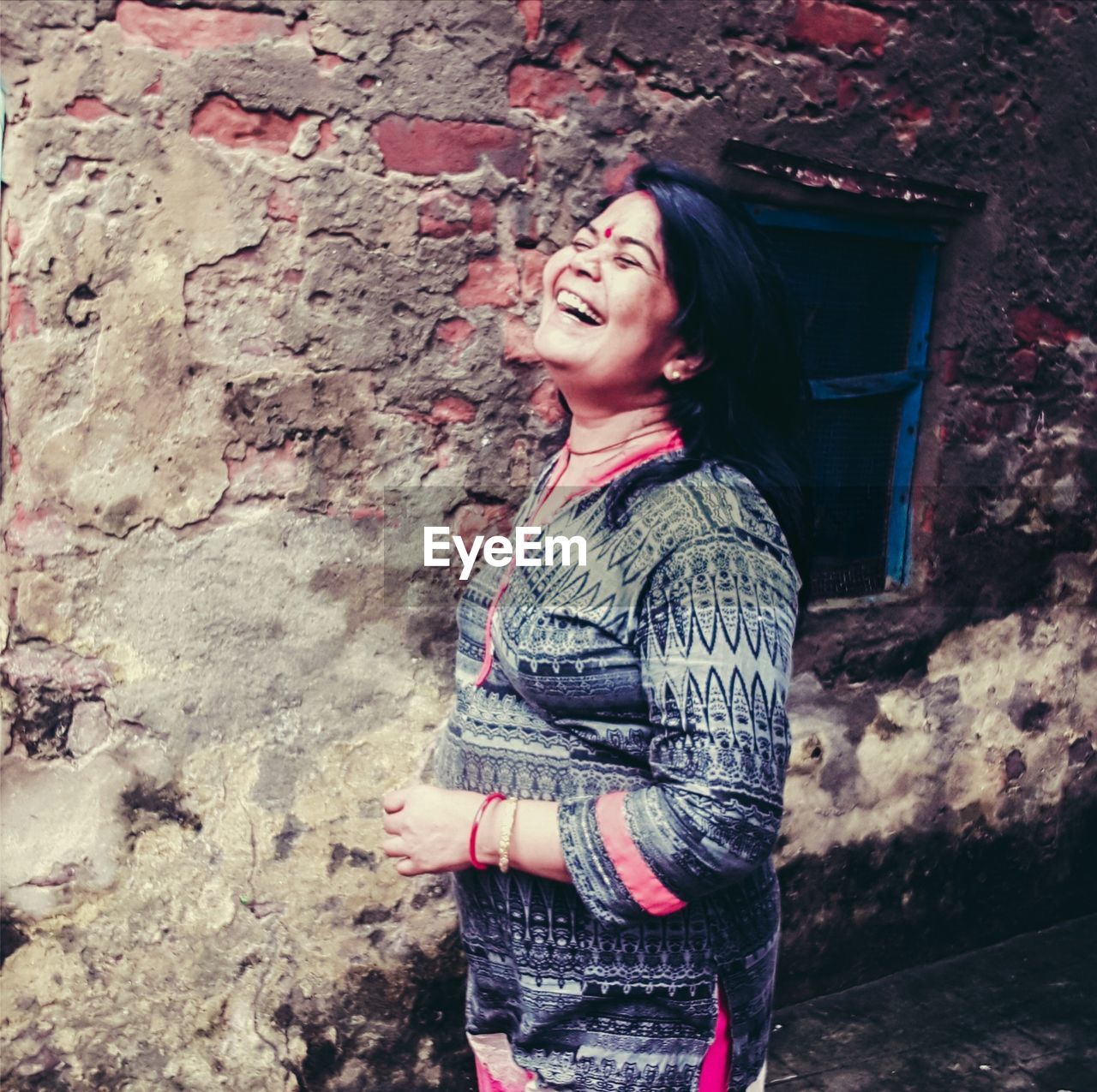 SMILING YOUNG WOMAN STANDING AGAINST WALL