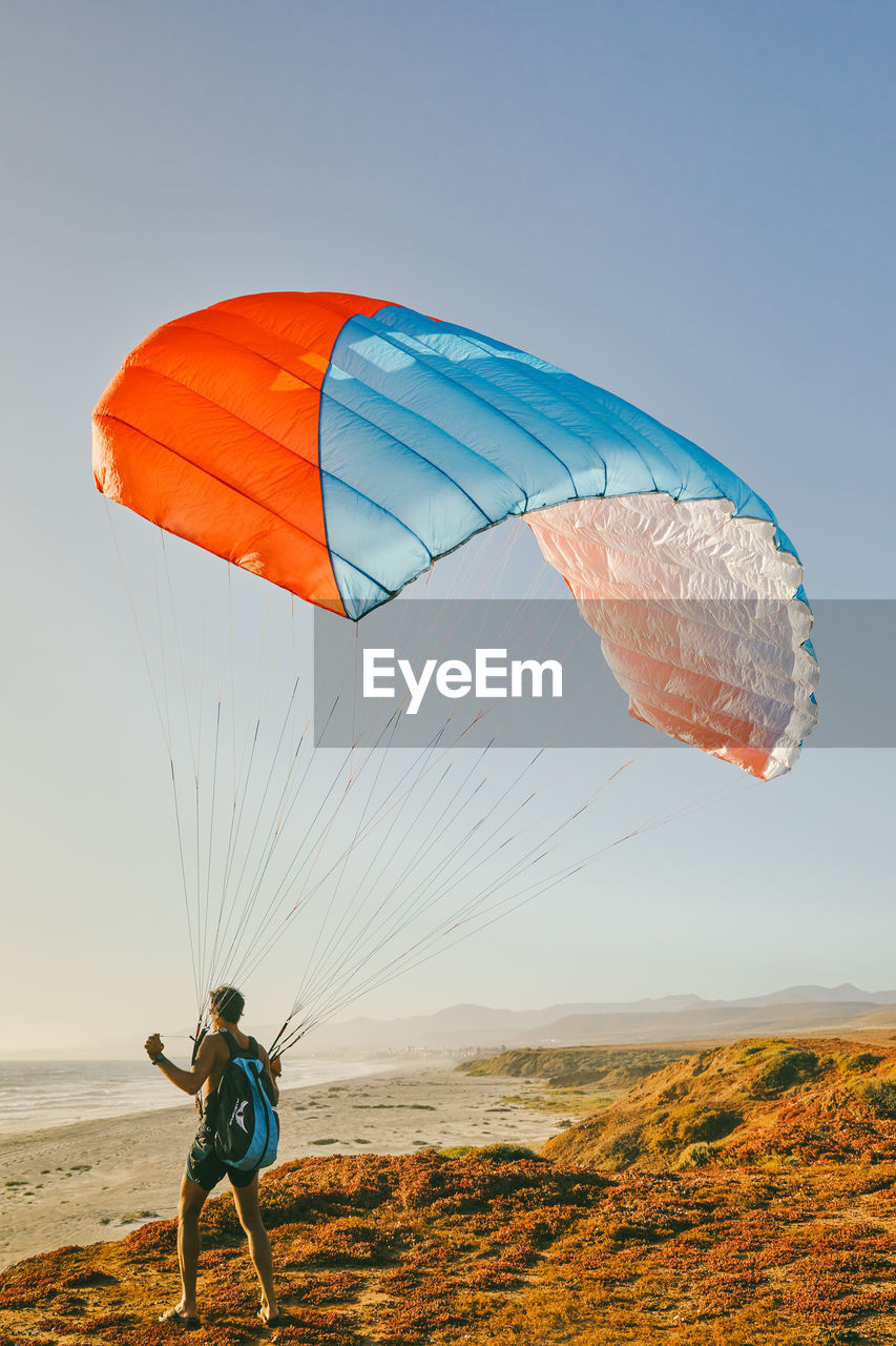 Young man paragliding during sunset off cliffs in baja, mexico.