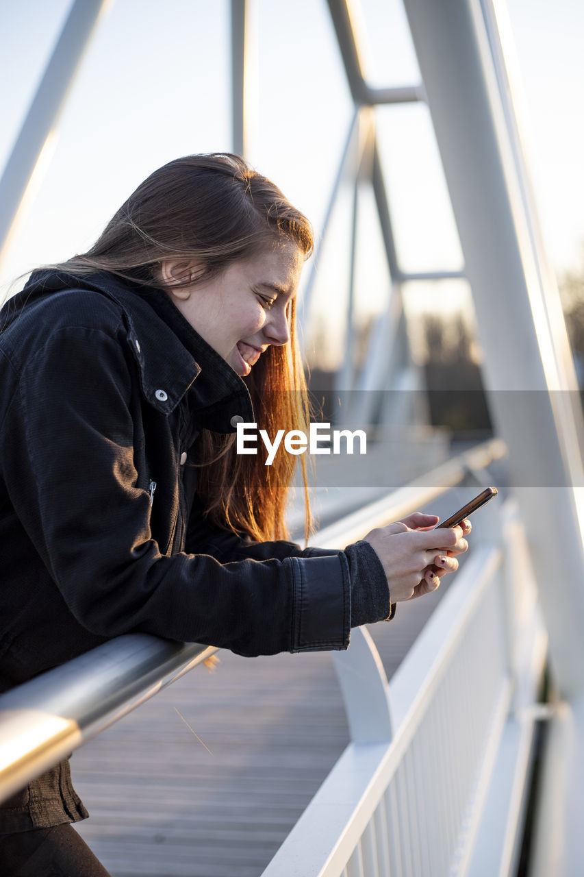 Young adult woman laughing in a footbridge with her phone