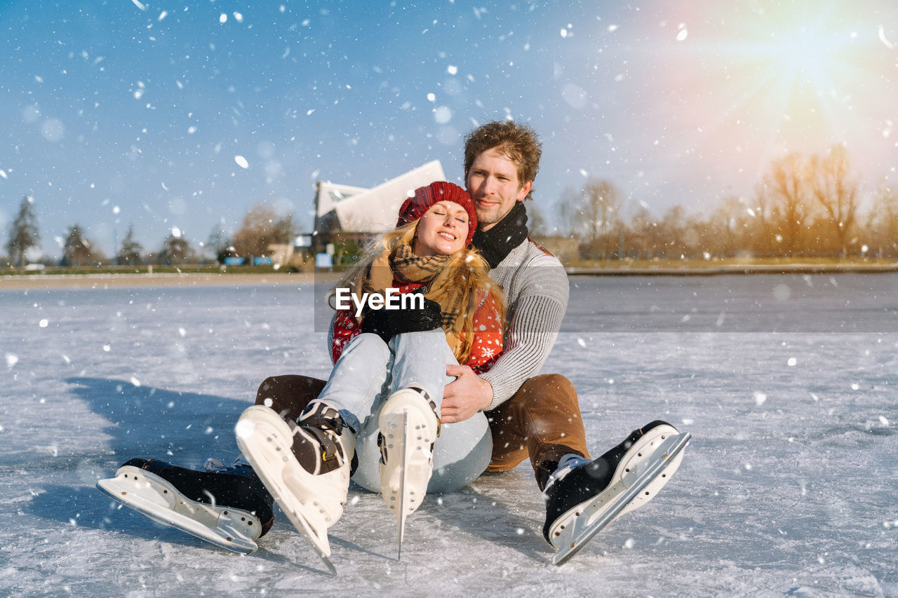 Couple wearing skaters sitting on frozen lake