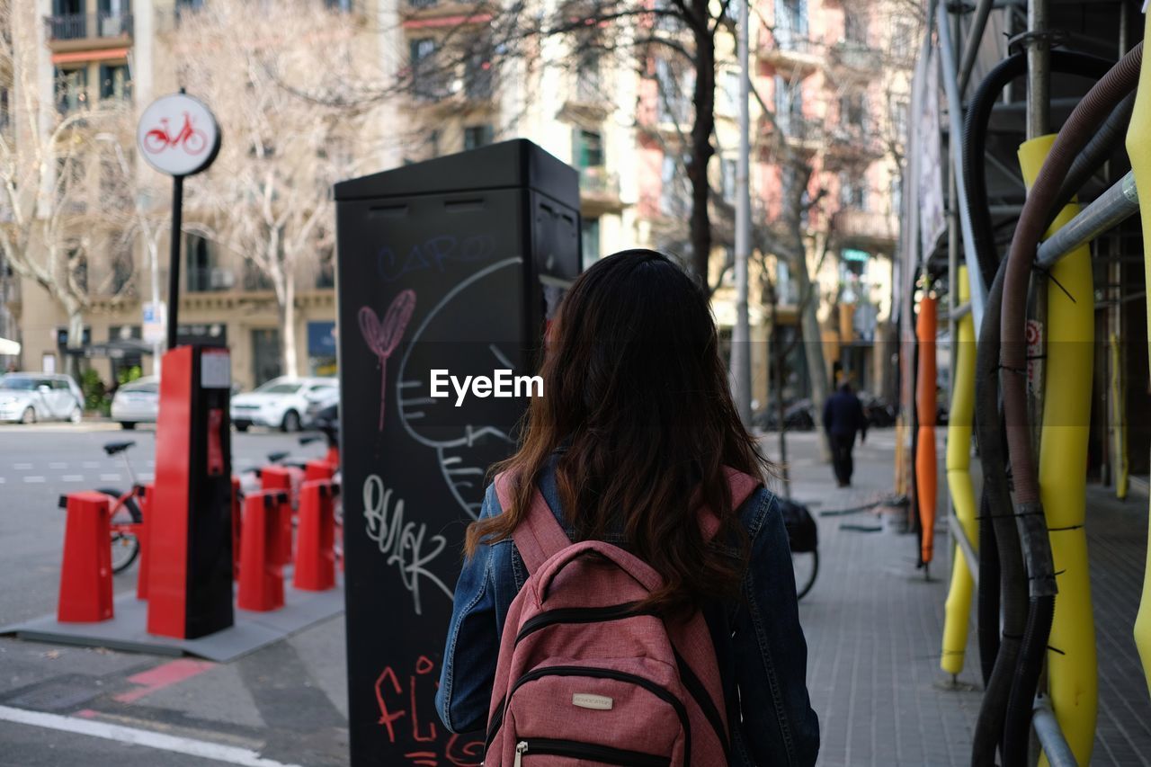 REAR VIEW OF WOMAN WALKING ON STREET