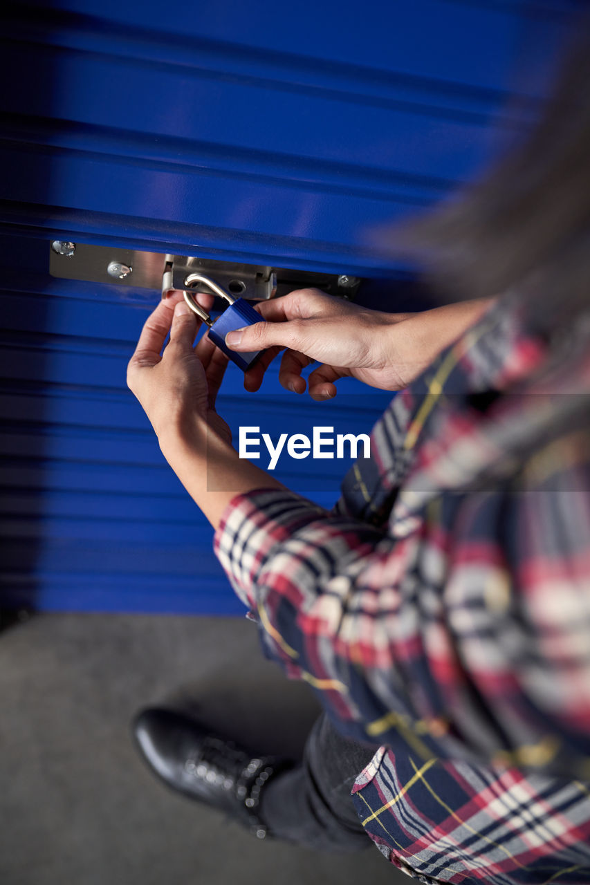 Anonymous cropped woman hands holding a blue padlock while closing it