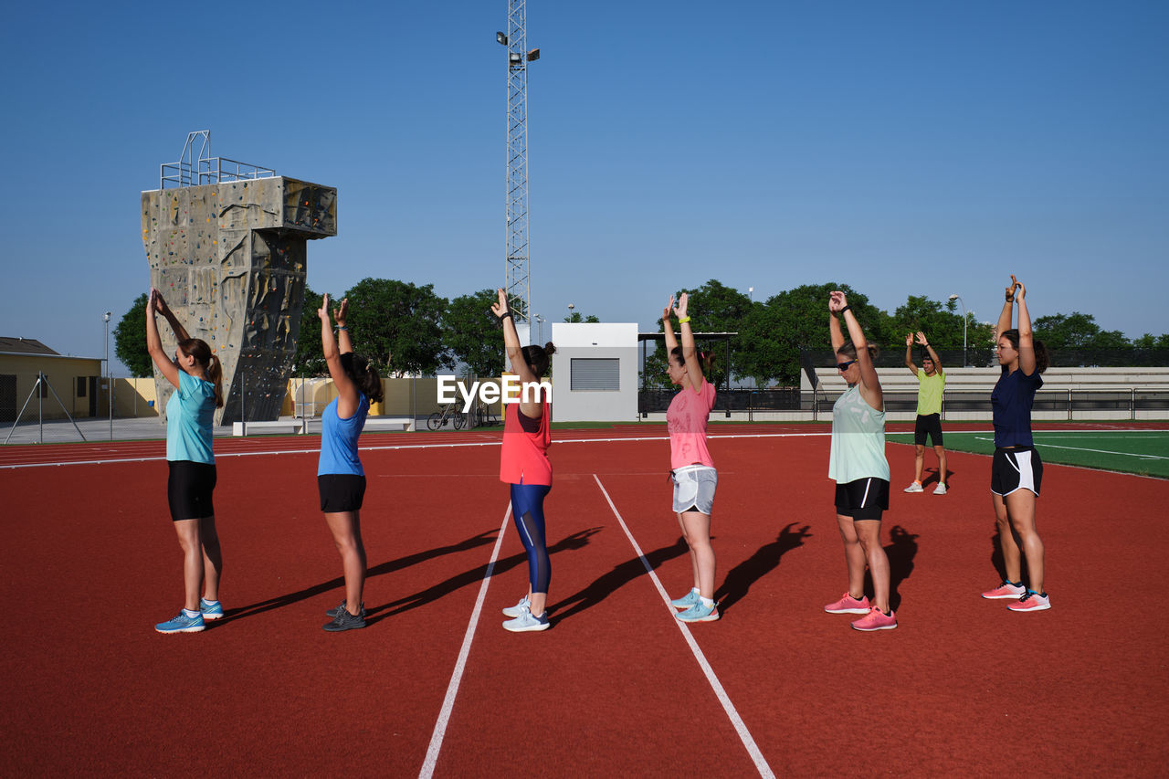 Group of women practice pre-workout stretching with their young traine