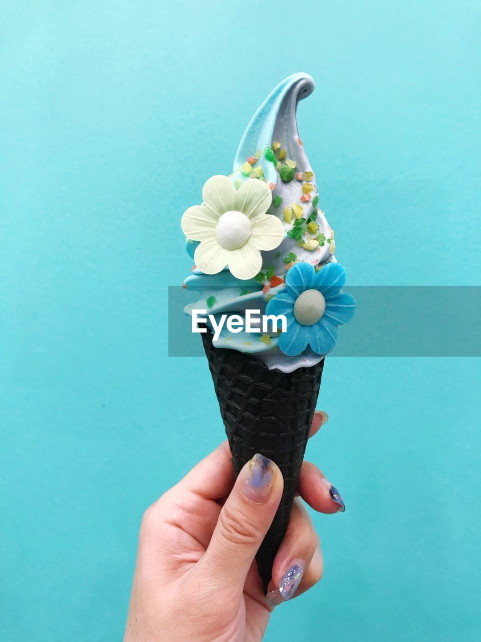 Close-up of hand holding ice cream against blue background