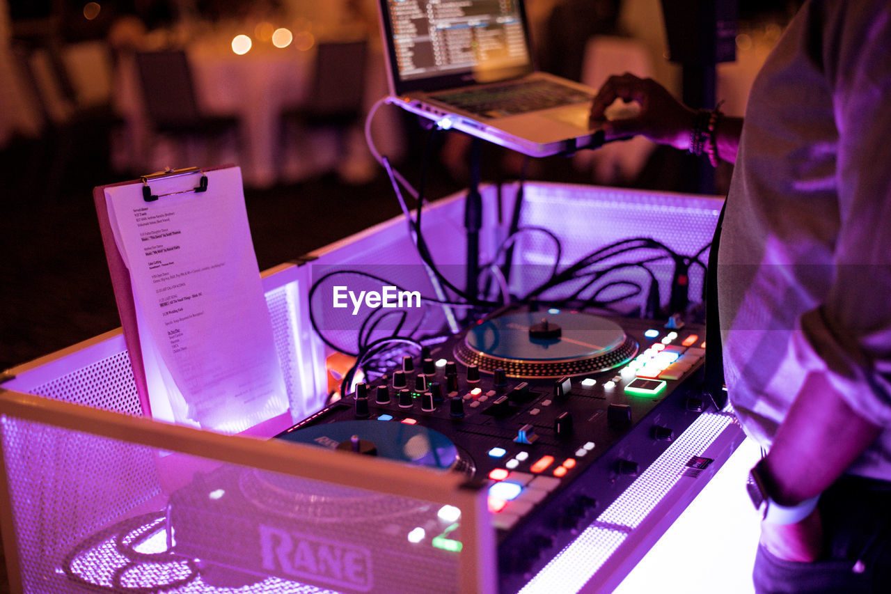 Close up of dj console at the party. neon lights over the hands of playing at wedding.