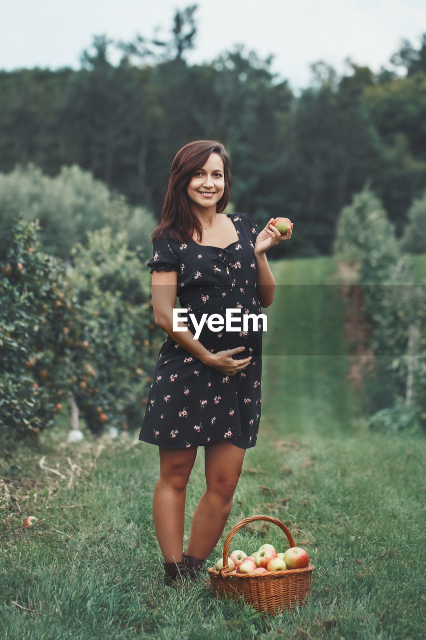 Portrait of pregnant woman holding apple standing at farm