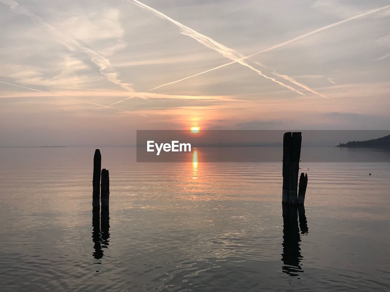 Wooden posts in sea against sky during sunset