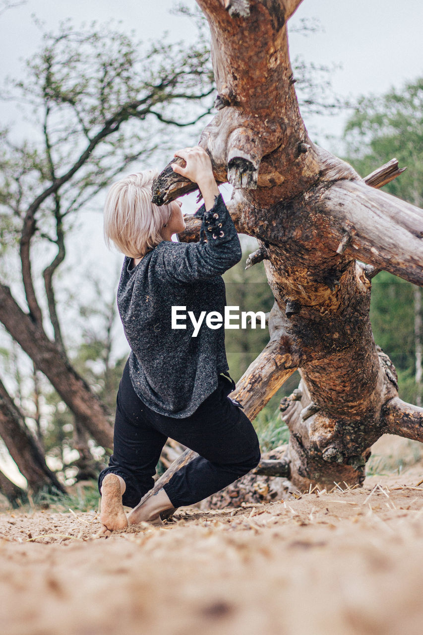 Full length of woman hanging on fallen tree at forest