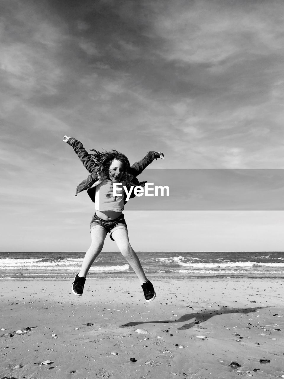 Full length of girl jumping on beach against sky