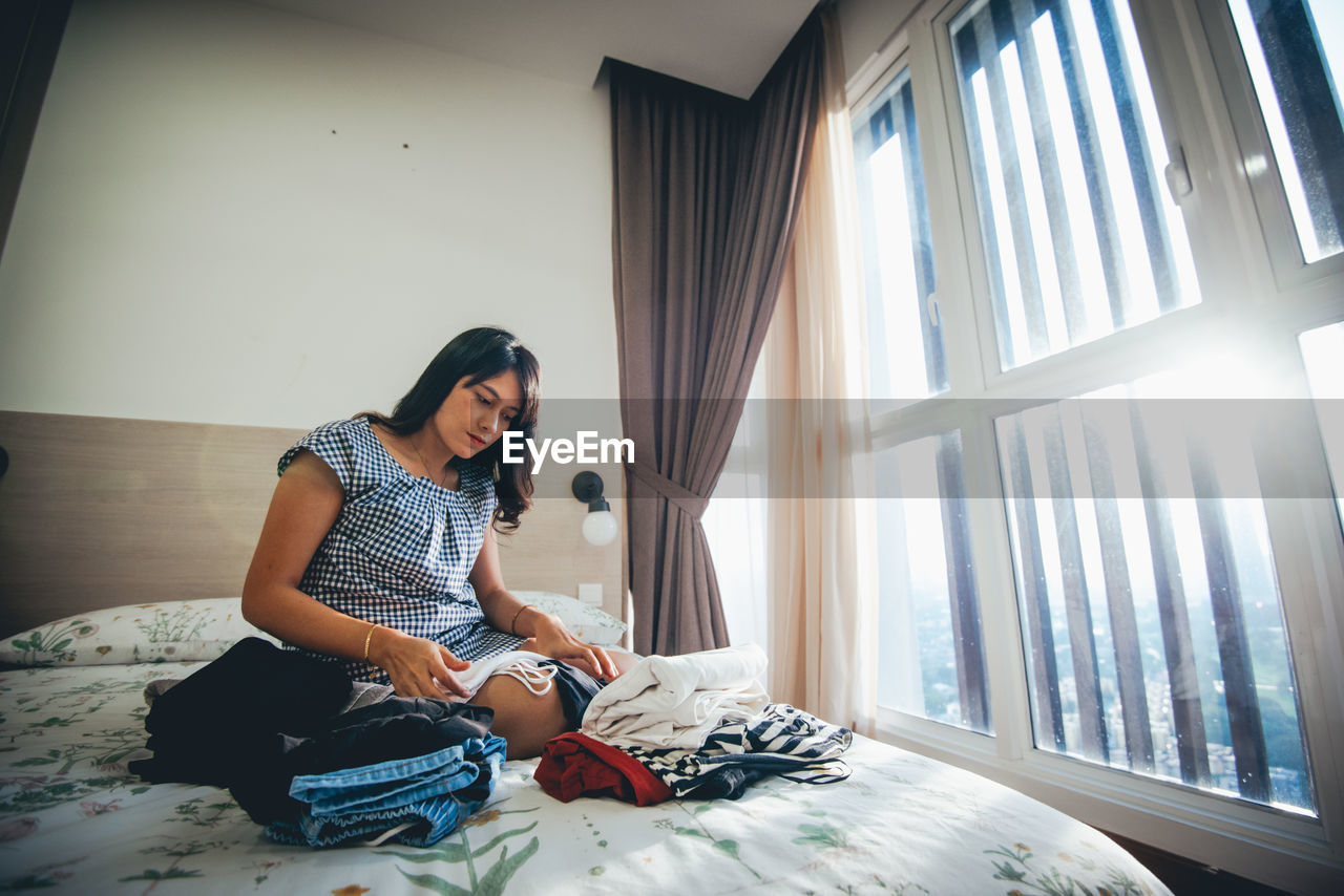 Young woman folding cloth on bed at home